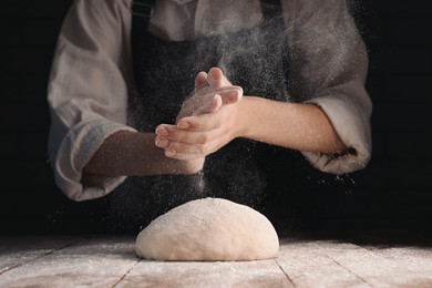 Photo of Woman making dough at wooden table on dark background, closeup