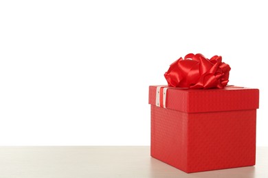 Red gift box with bow on wooden table against white background, space for text