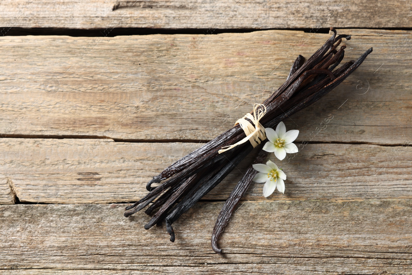 Photo of Bunch of vanilla pods and flowers on wooden table, top view. Space for text