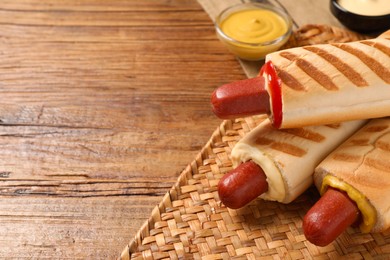 Photo of Tasty french hot dogs with different sauces on wooden table, closeup. Space for text