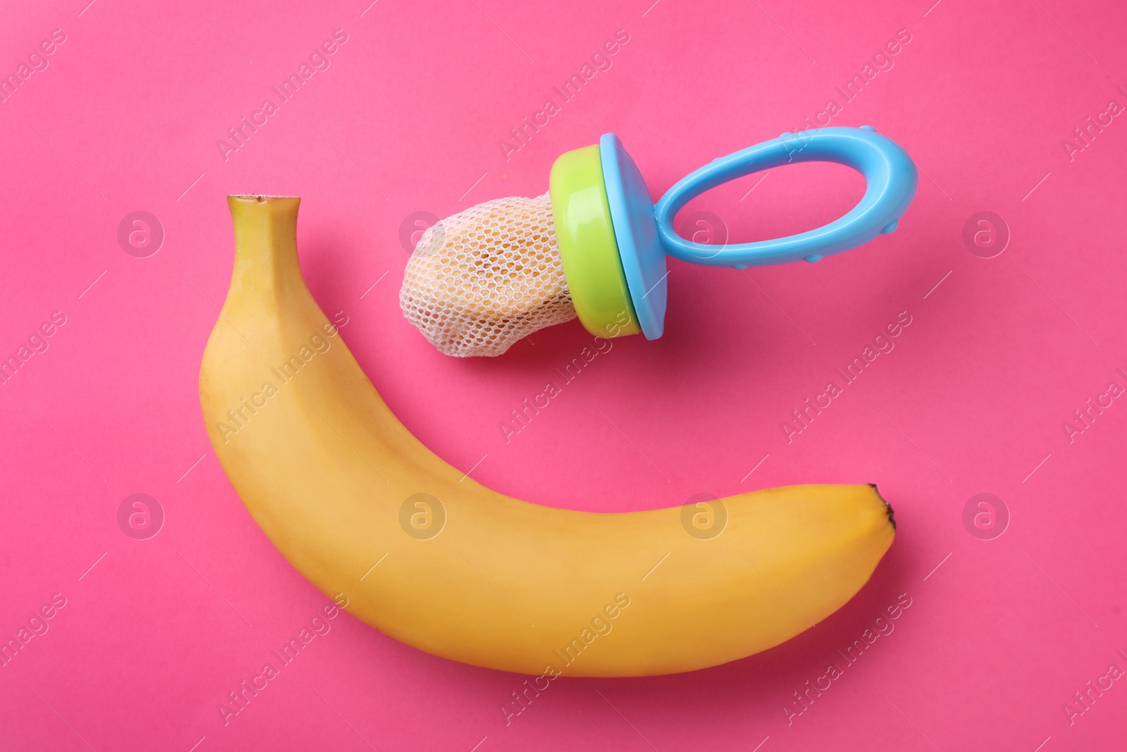 Photo of Nibbler with fresh banana on pink background, flat lay. Baby feeder