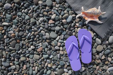 Photo of Stylish lilac flip flops and sea shell on stones outdoors, flat lay. Space for text