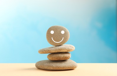Photo of Stackstones with drawn happy face on beige table against light blue background. Zen concept