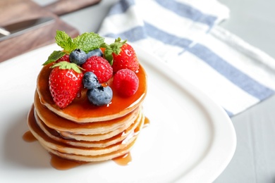 Tasty pancakes with berries and syrup on plate