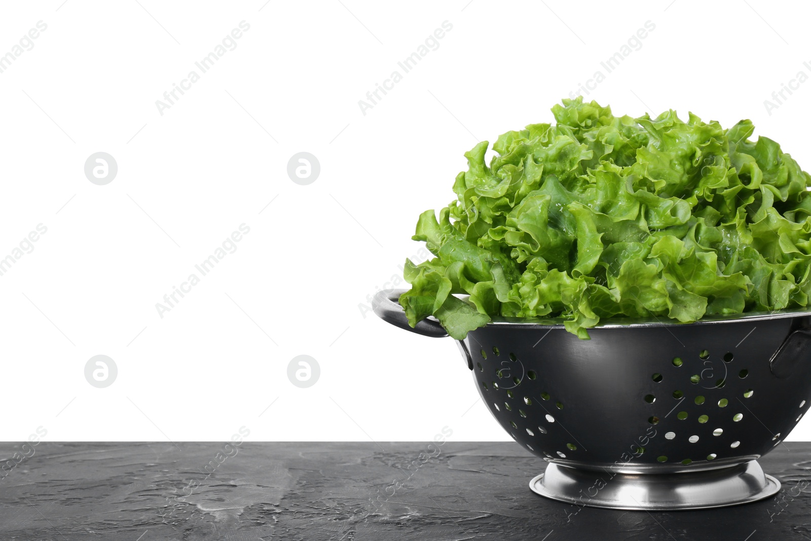 Photo of Metal colander with fresh lettuce on black textured table against white background, space for text