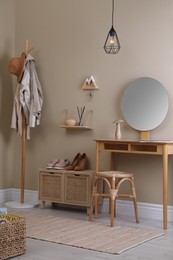 Photo of Modern hallway interior with stylish furniture, round mirror and wooden hanger for keys on beige wall