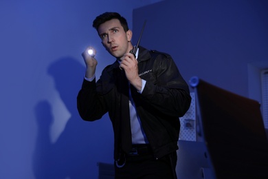 Male security guard with flashlight and portable radio transmitter in dark room