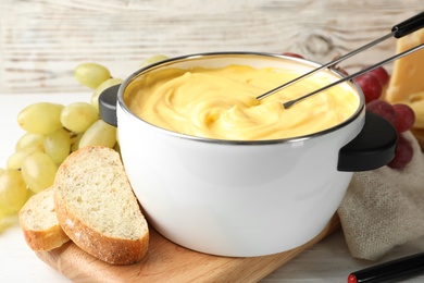 Photo of Pot with delicious cheese fondue and forks on wooden table