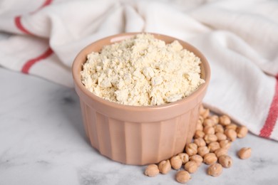 Chickpea flour in bowl and seeds on white marble table