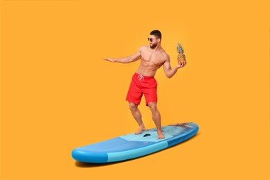 Photo of Man with pineapple posing on SUP board against orange background