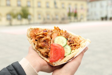 Woman holding delicious bread with roasted meat and vegetables outdoors, closeup. Street food