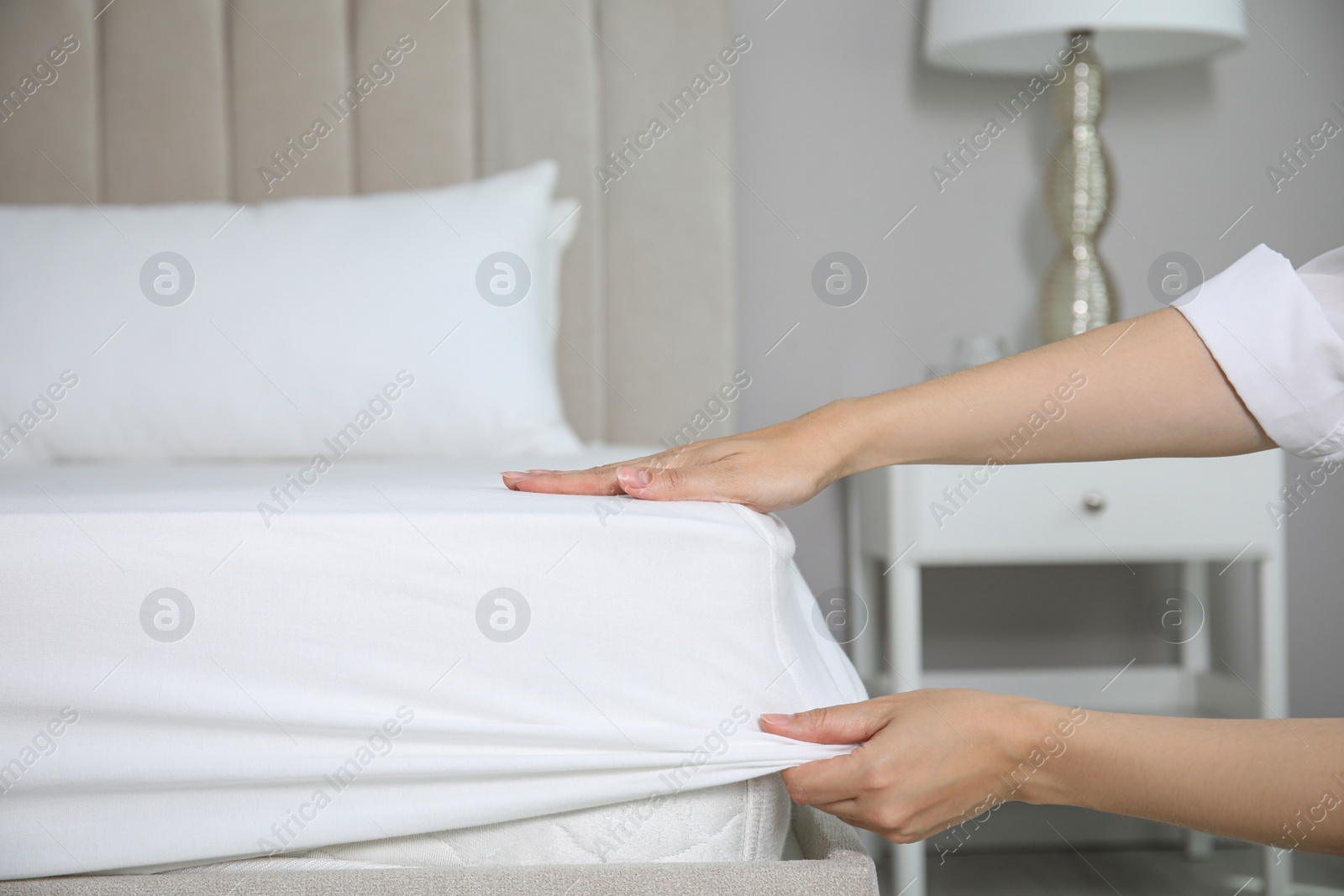 Photo of Woman putting white fitted sheet over mattress on bed indoors, closeup