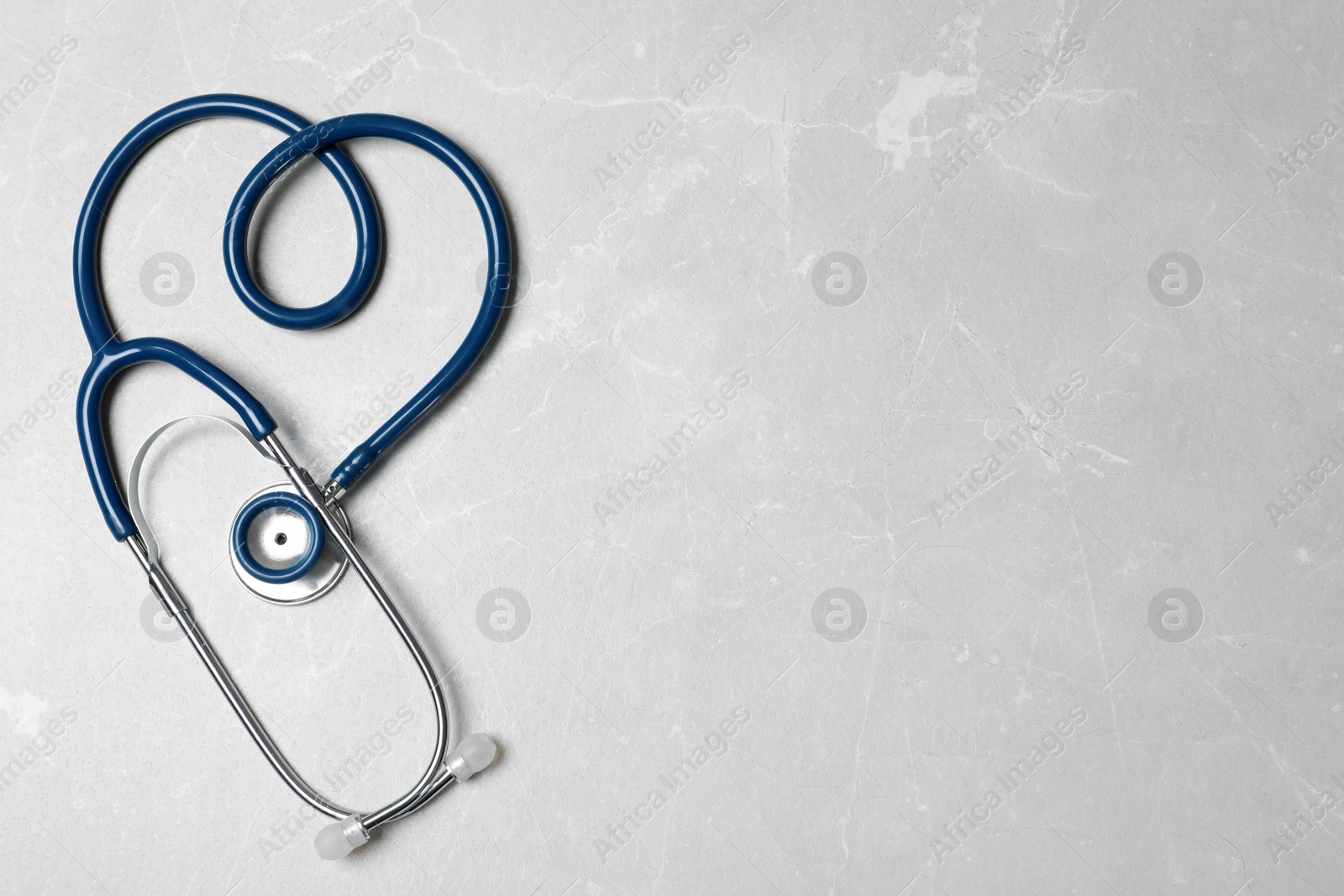 Photo of Stethoscope folded in shape of heart on light background, top view. Space for text
