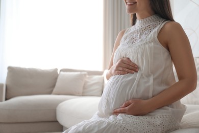 Photo of Pregnant young woman touching belly at home, closeup. Space for text