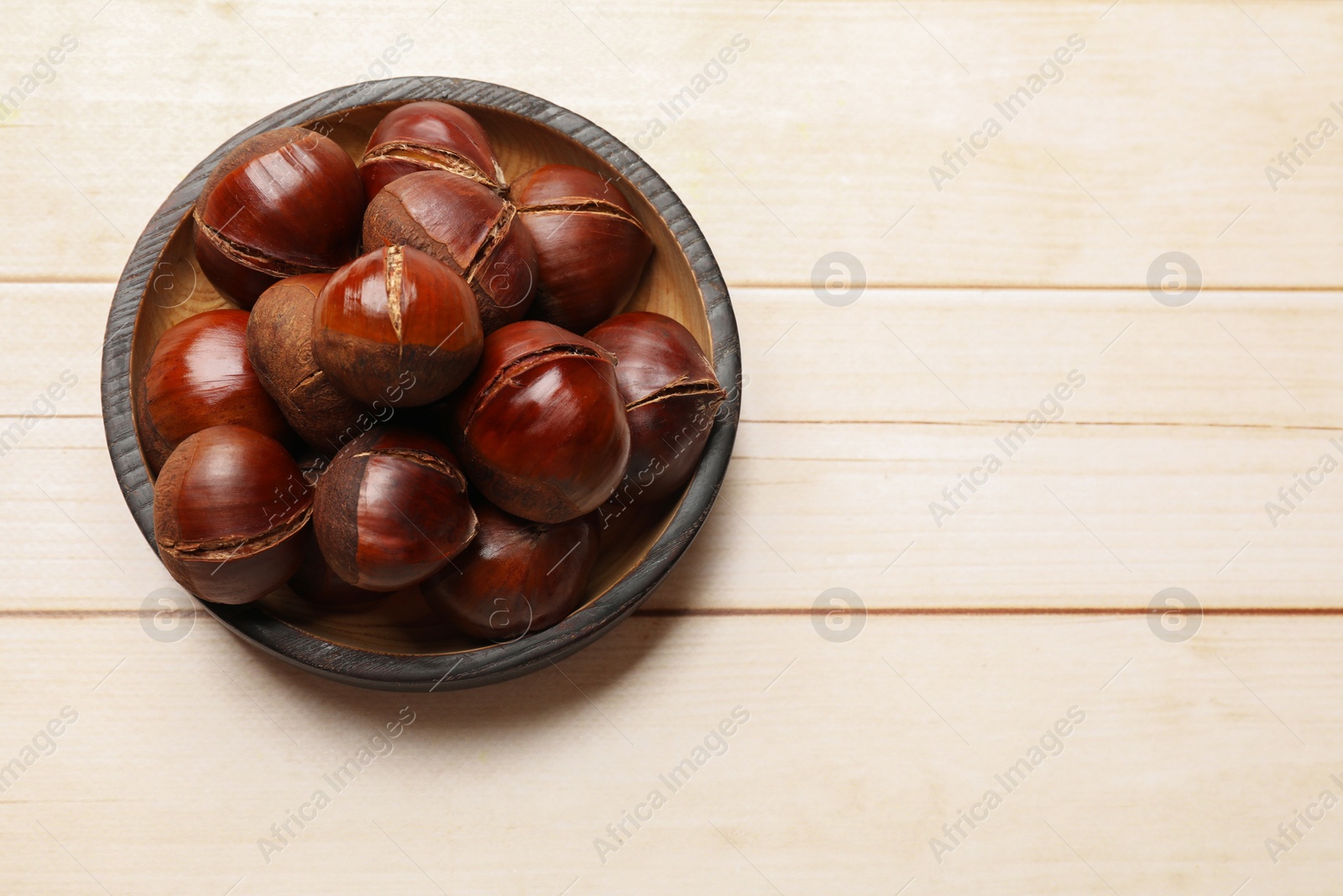 Photo of Roasted edible sweet chestnuts on wooden table, top view. Space for text
