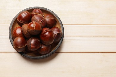 Photo of Roasted edible sweet chestnuts on wooden table, top view. Space for text