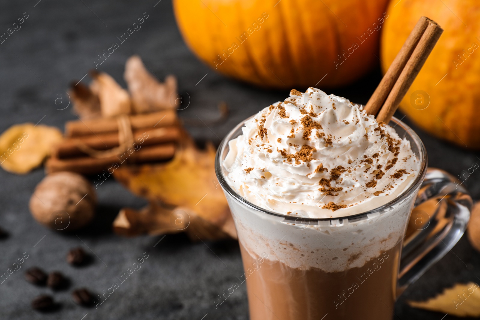 Photo of Pumpkin spice latte with whipped cream and cinnamon stick in glass cup on grey table, closeup. Space for text