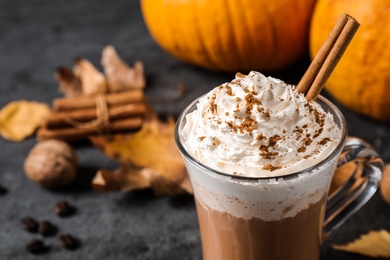 Photo of Pumpkin spice latte with whipped cream and cinnamon stick in glass cup on grey table, closeup. Space for text