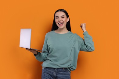 Photo of Cheerful woman with laptop on orange background
