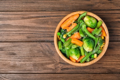 Photo of Bowl with different frozen vegetables on wooden table, top view
