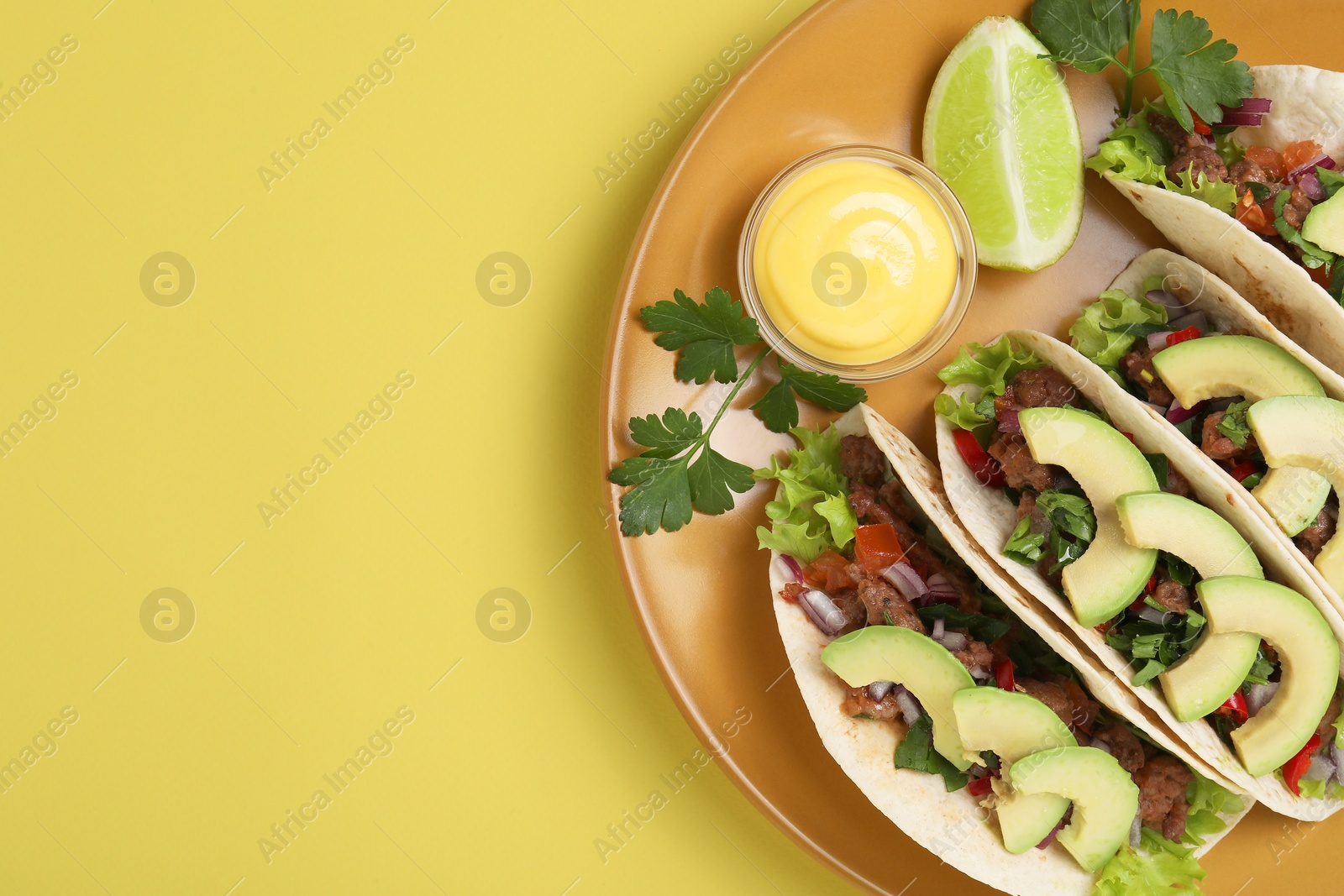 Photo of Delicious tacos with meat, vegetables and avocado served on yellow table, top view. Space for text