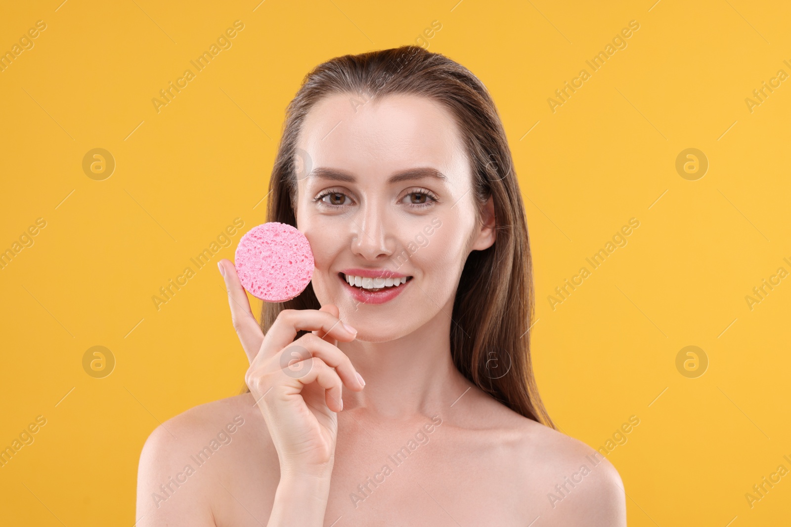 Photo of Happy young woman holding face sponge on orange background