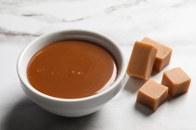 Photo of Yummy salted caramel in bowl and candies on white marble table