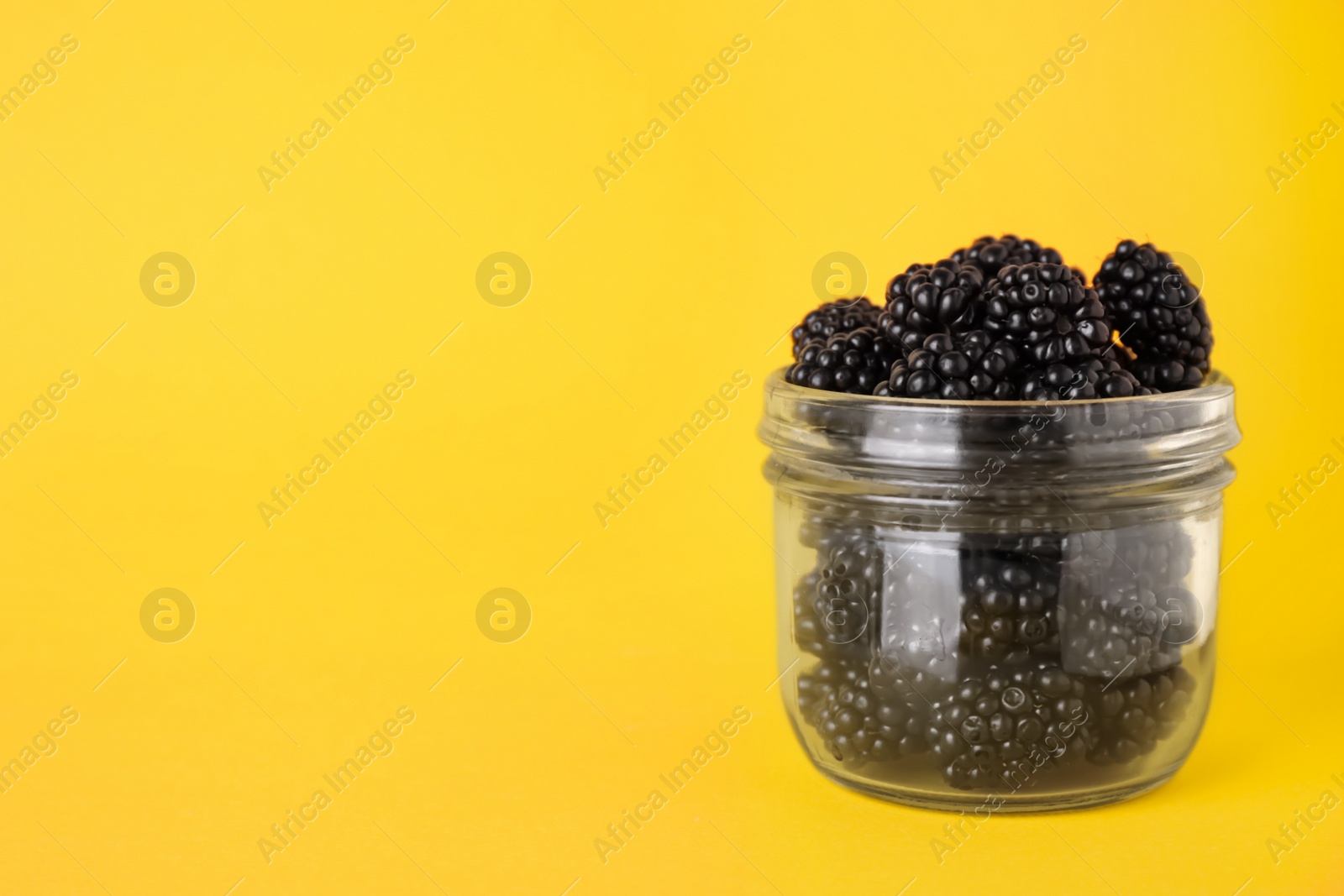 Photo of Fresh ripe blackberries in glass jar on orange background. Space for text