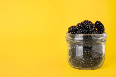 Photo of Fresh ripe blackberries in glass jar on orange background. Space for text