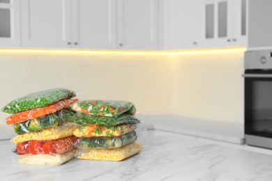 Plastic bags with different frozen vegetables on white marble table in kitchen. Space for text