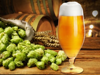 Image of Glass of tasty light beer, fresh hops and wheat spikes on wooden table in cellar