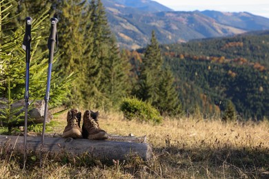 Photo of Pair of trekking poles and hiking boots in mountains on sunny day, space for text