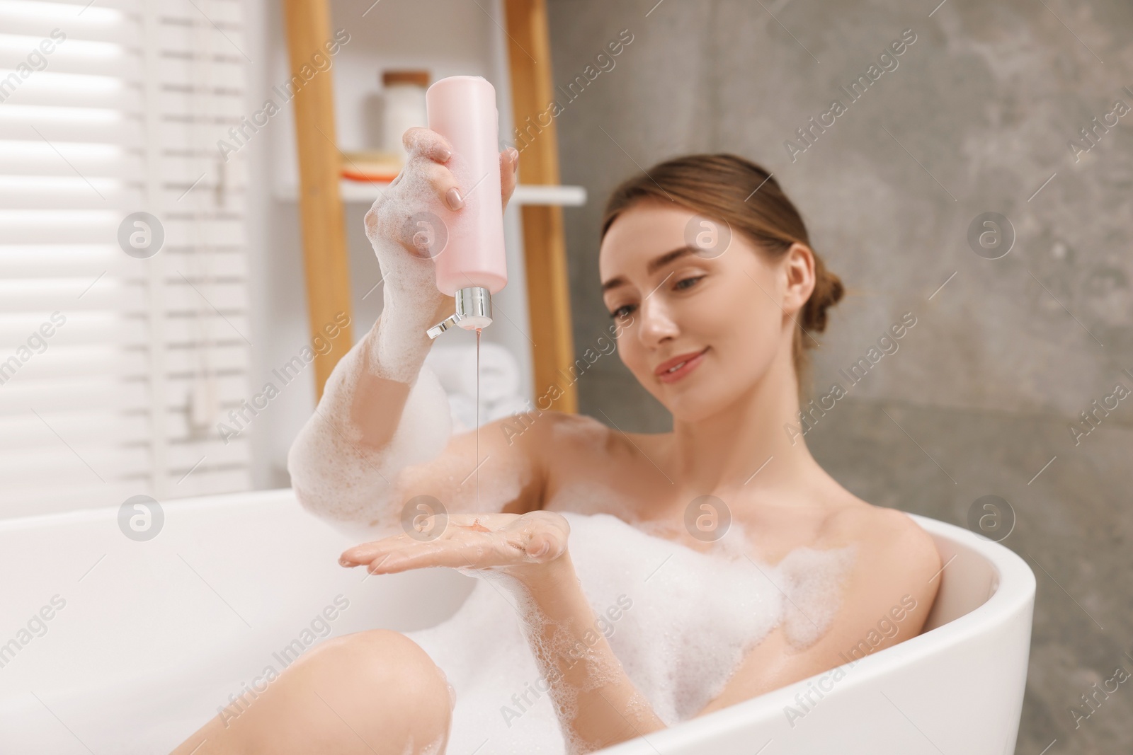 Photo of Woman pouring shower gel onto hand in bath indoors