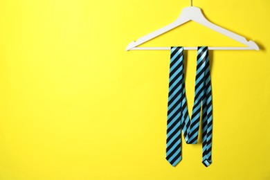 Photo of Hanger with striped necktie on yellow background. Space for text