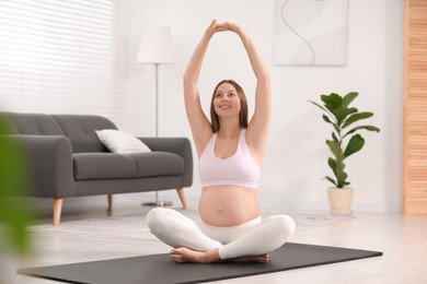 Pregnant woman doing exercises on yoga mat at home