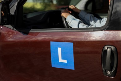 Photo of Learner driver driving car with L-plate, view from outside. Driving school