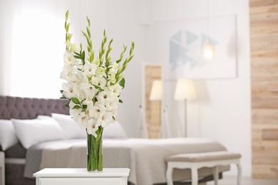 Photo of Vase with beautiful white gladiolus flowers on wooden table in bedroom. Space for text