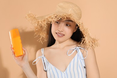 Beautiful young woman in straw hat holding sun protection cream on beige background