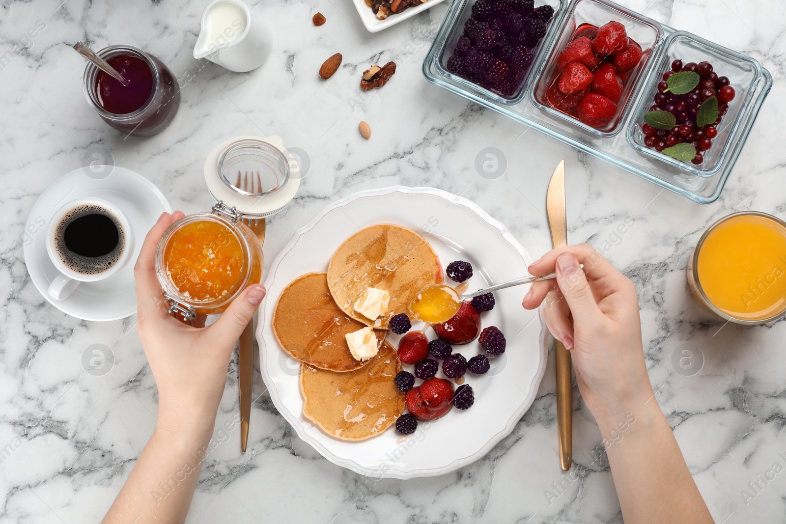 Photo of Woman eating delicious pancakes with berries and butter at table