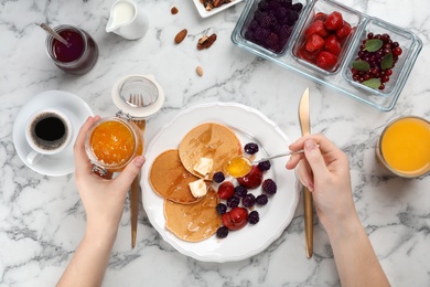 Photo of Woman eating delicious pancakes with berries and butter at table