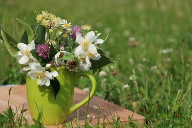 Green cup with different wildflowers and herbs on wooden board in meadow. Space for text