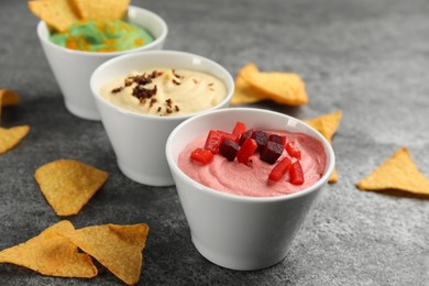 Photo of Different kinds of tasty hummus with ingredients on grey table