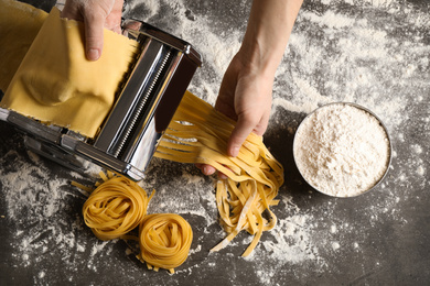 Woman preparing noodles with pasta maker machine at grey table, top view