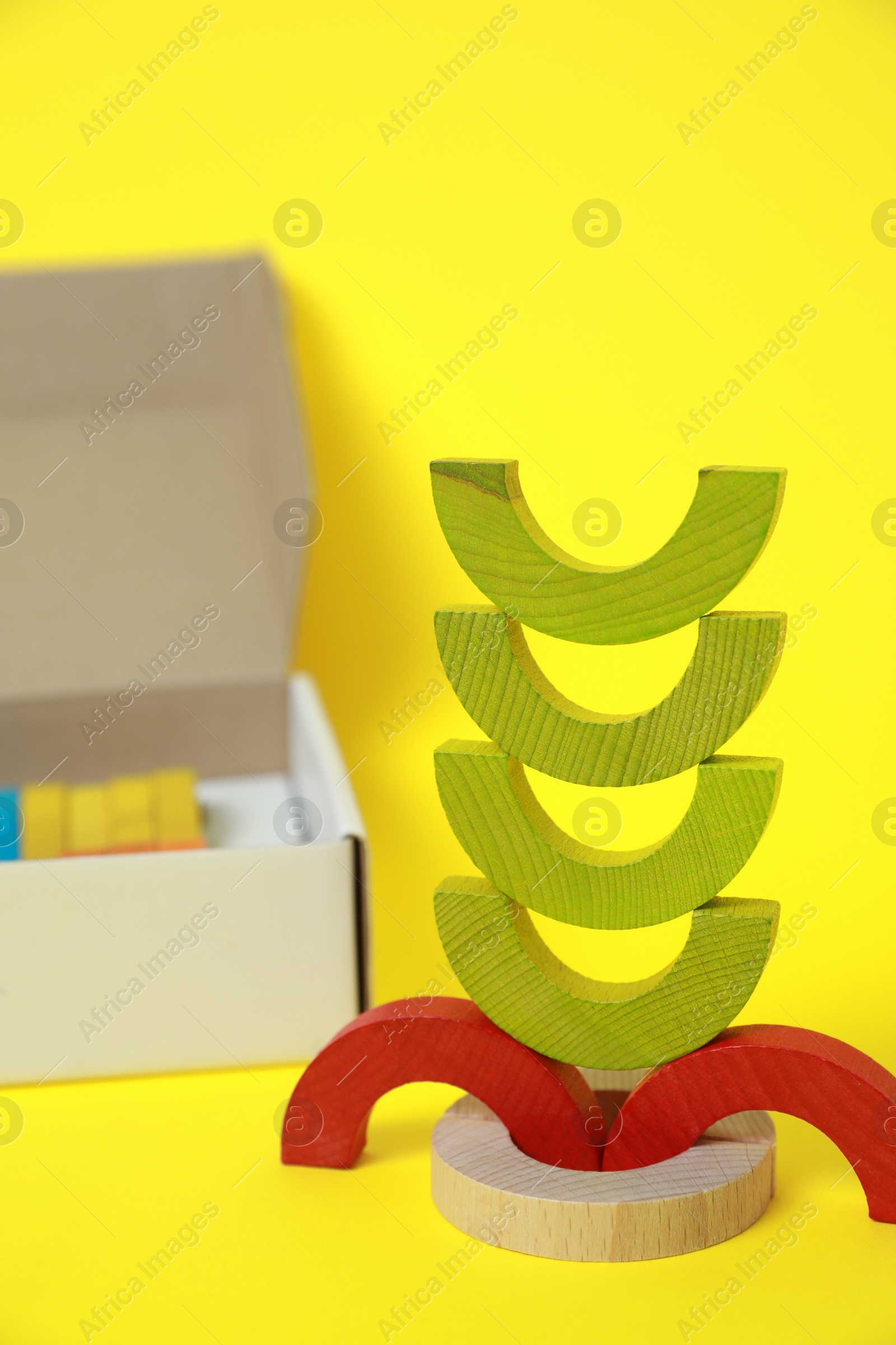 Photo of Colorful wooden pieces of playing set and box on yellow background. Educational toy for motor skills development