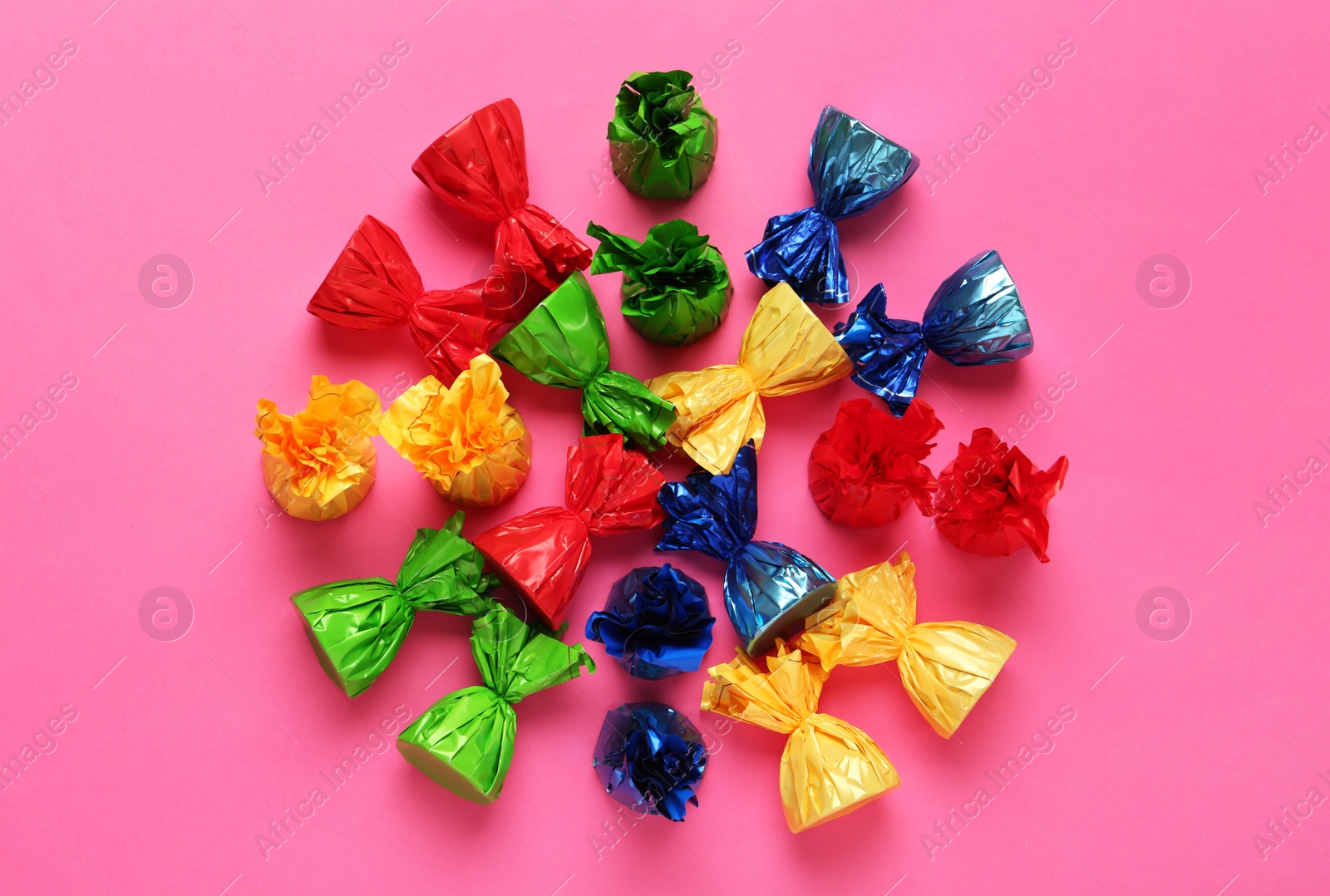 Photo of Candies in colorful wrappers on pink background, flat lay