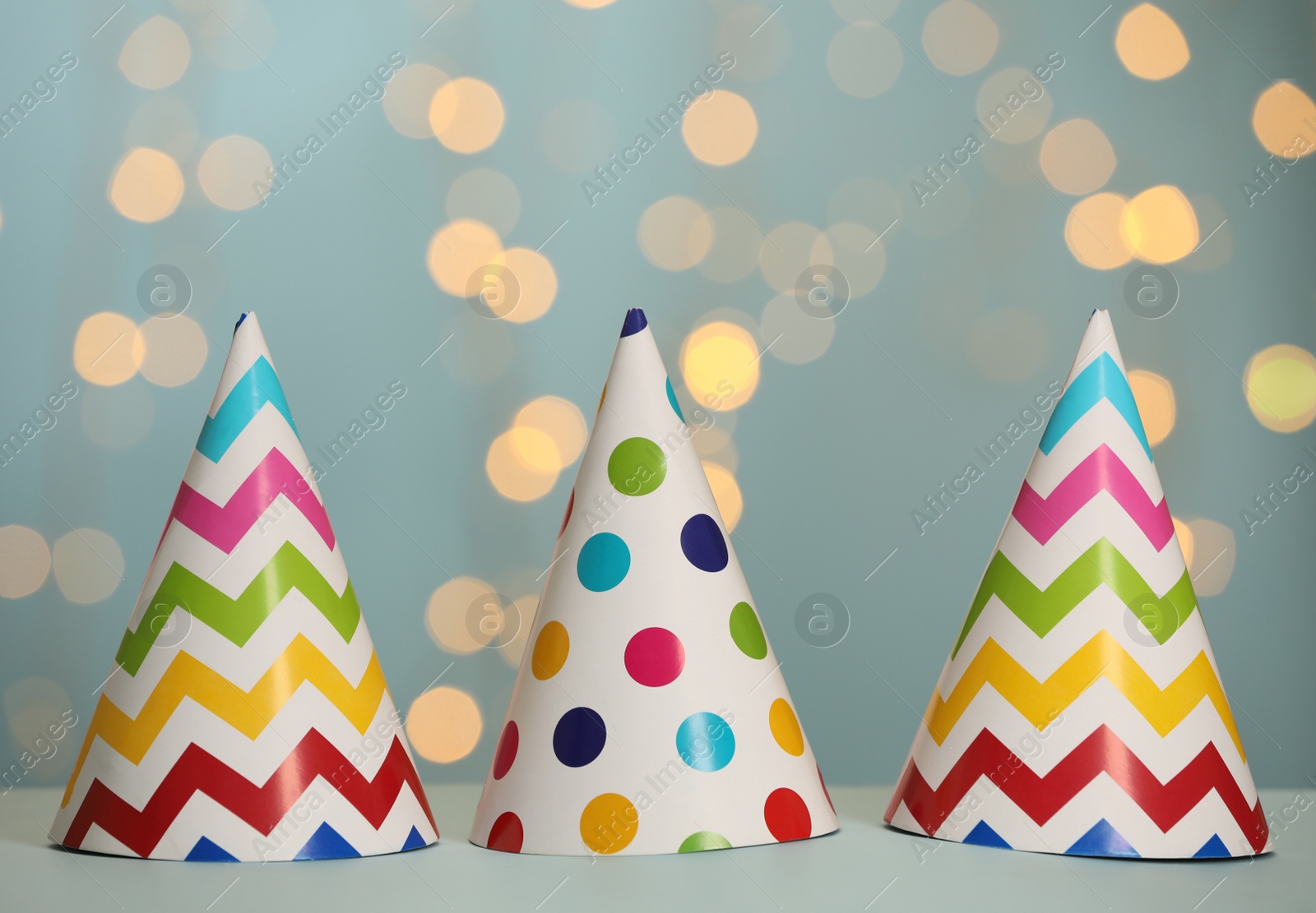 Photo of Beautiful party hats on light blue table against blurred festive lights