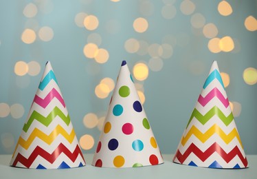 Beautiful party hats on light blue table against blurred festive lights