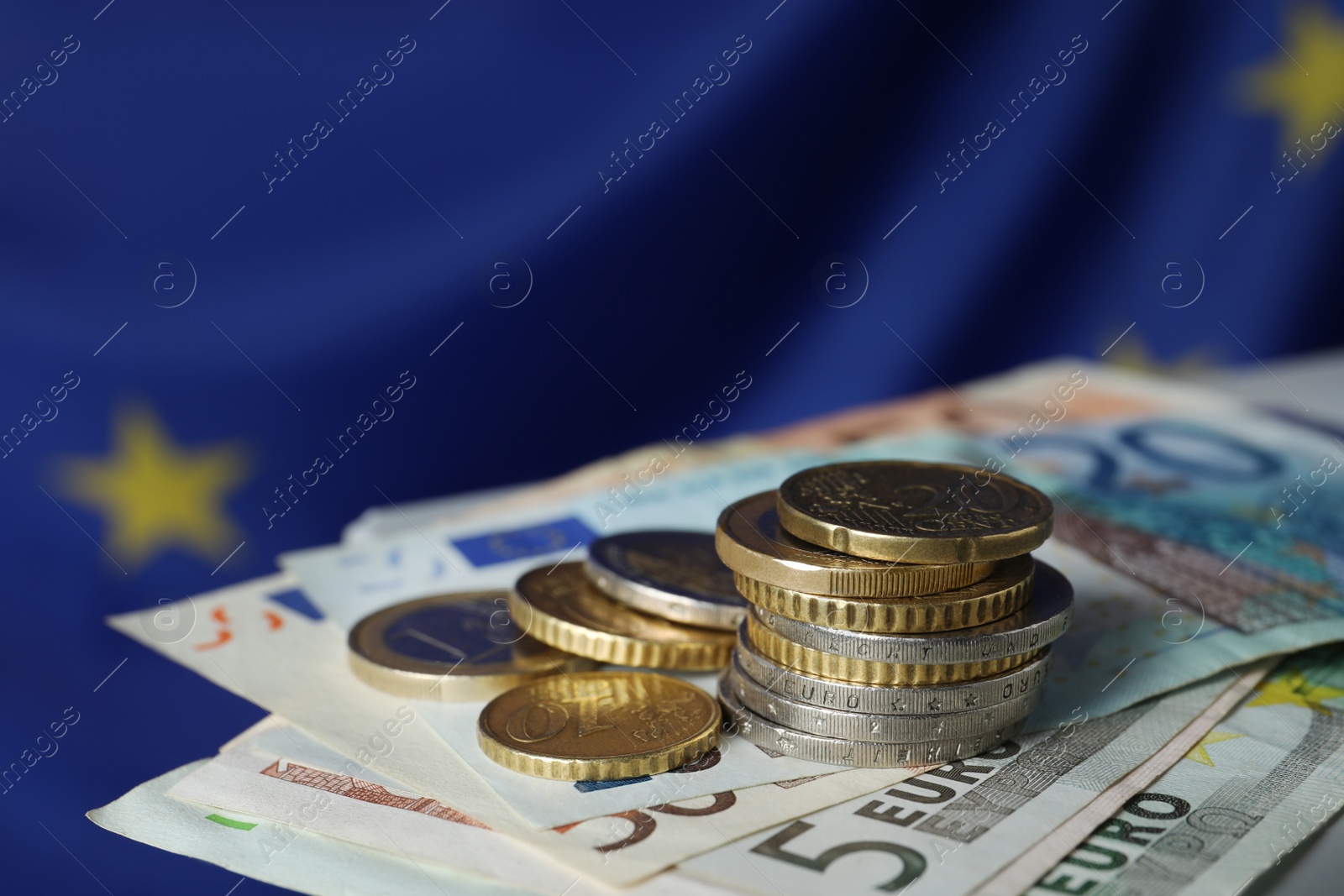 Photo of Coins and banknotes on table against European Union flag, closeup. Space for text