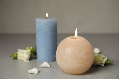 Photo of Burning candles and beautiful flowers on grey table