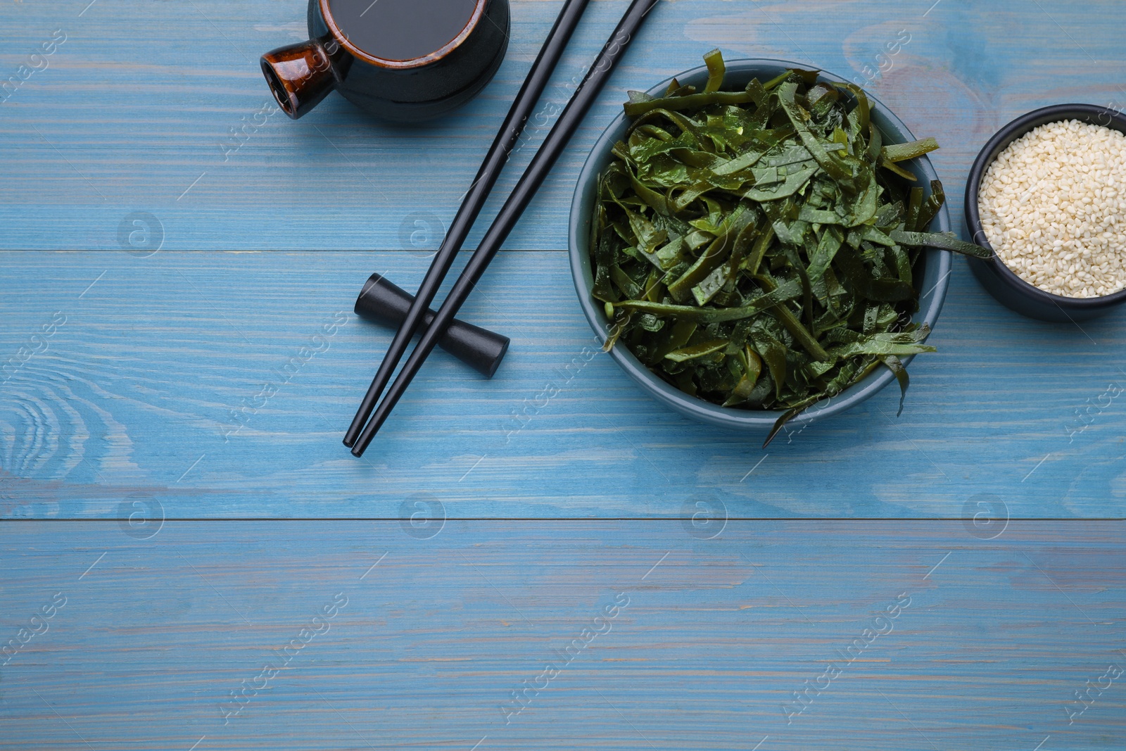 Photo of Fresh laminaria (kelp) seaweed served on light blue wooden table, flat lay. Space for text